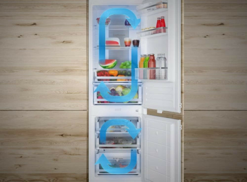 Otwarta lodówka z widocznymi półkami wypełnionymi jedzeniem i napojami, z niebieskimi strzałkami symbolizującymi przepływ powietrza. Wnętrze lodówki zawiera owoce, warzywa, butelki i pojemniki.