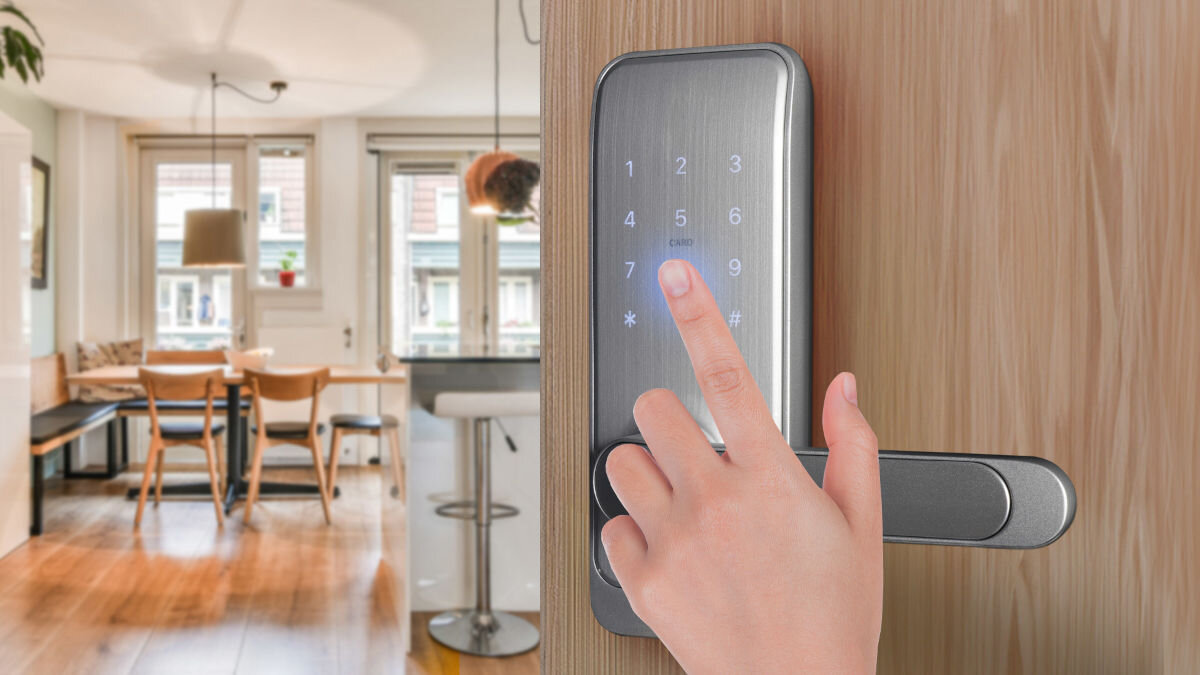 Na drewnianych drzwiach zamontowana jest srebrna klamka z panelem dotykowym, na którym widoczne są cyfry od 1 do 9 oraz symbole * i #. W tle znajduje się wnętrze mieszkania z jadalnią i kuchnią.