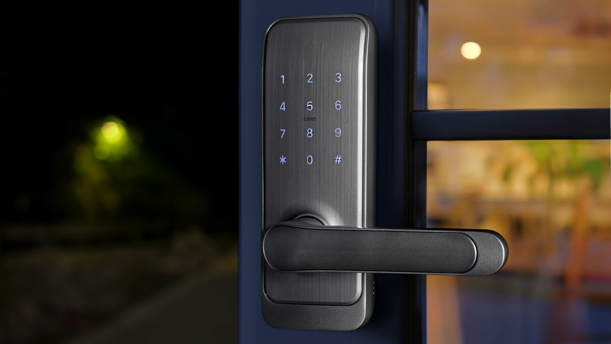 Srebrna klamka z panelem numerycznym, na którym widoczne są cyfry od 1 do 9 oraz symbole * i #. W tle rozmyte światła wnętrza budynku.