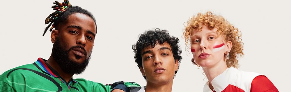 Trzy osoby stoją obok siebie, każda z nich ma na sobie kolorowy strój. Jedna z osób ma na twarzy namalowane czerwone paski.