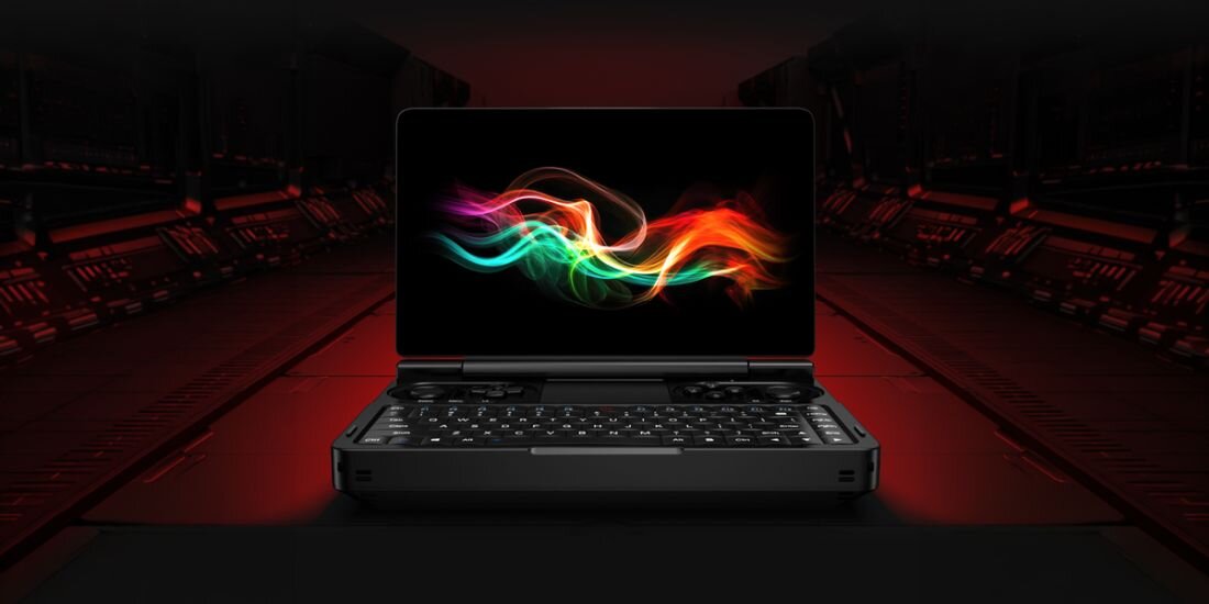 Na obrazie widoczny jest otwarty laptop z kolorową grafiką na ekranie, umieszczony na tle ciemnego, futurystycznego wnętrza. Klawiatura laptopa jest podświetlona, a całość utrzymana w ciemnej kolorystyce z czerwonymi akcentami.