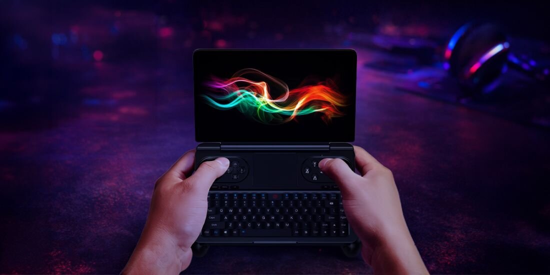 Osoba trzyma mały laptop z otwartym ekranem, na którym widoczna jest kolorowa grafika. Klawiatura urządzenia jest podświetlona, a w tle widać rozmyte światła.