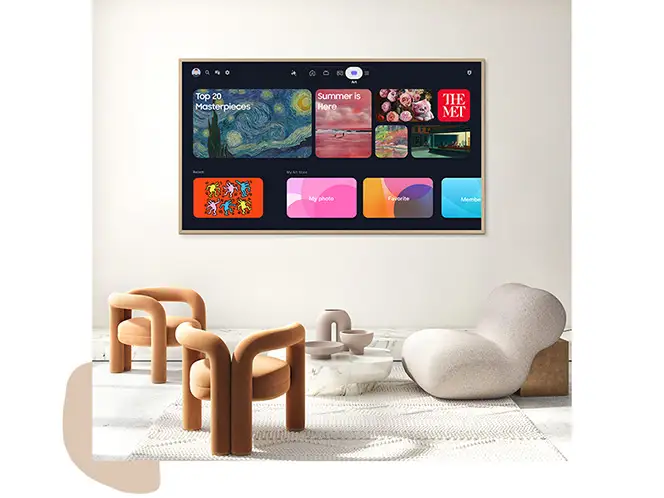 Na ścianie wisi duży telewizor z wyświetlonym interfejsem użytkownika, na którym widoczne są różne aplikacje i obrazy. Przed telewizorem znajdują się nowoczesne fotele i stolik na jasnej podłodze.