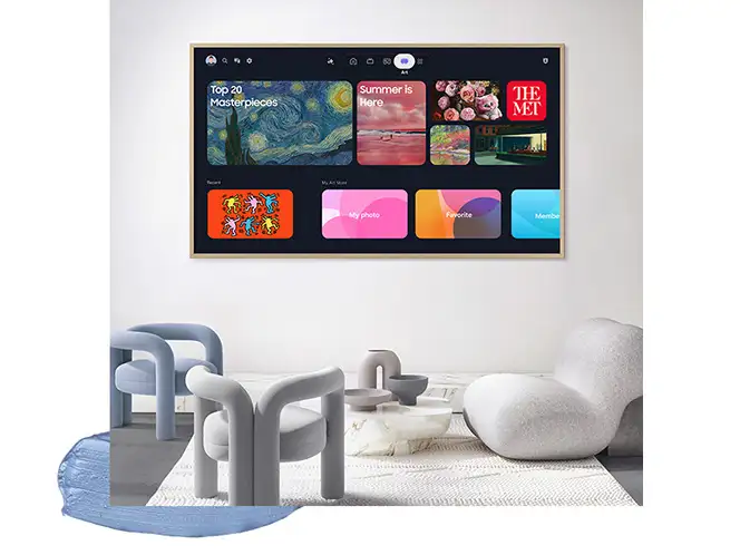 Na ścianie wisi duży telewizor z wyświetlonym interfejsem aplikacji, w tym miniaturami obrazów i tekstami takimi jak \'Top 20 Masterpieces\' i \'Summer is Here\'. Przed telewizorem znajduje się nowoczesny zestaw mebli z krzesłami i stolikiem na jasnym dywanie.