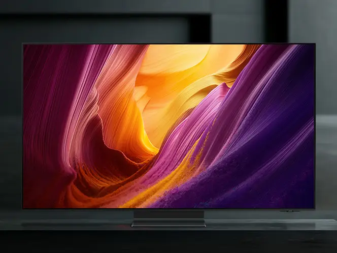 2026-oled-infinity-one-design 664x498 Telewizor wyświetla kolorową grafikę z dominującymi odcieniami fioletu, pomarańczu i żółci. Urządzenie stoi na ciemnym tle.