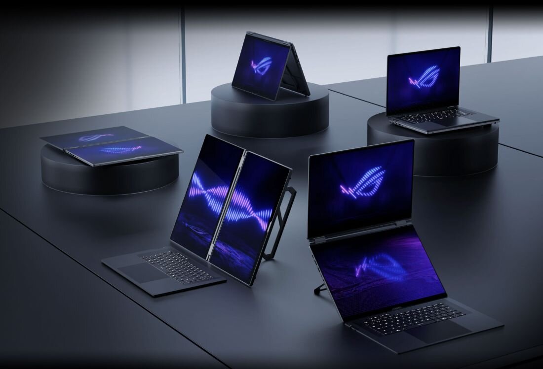 Na obrazie widać kilka laptopów ustawionych na czarnych, okrągłych podestach. Na ekranach laptopów wyświetla się logo producenta w formie stylizowanego oka z fioletowym motywem graficznym.