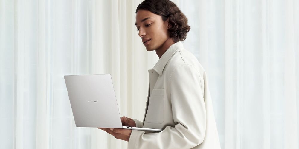 Osoba trzymająca otwarty laptop w jasnym pomieszczeniu. Na obudowie laptopa widoczne jest logo producenta.