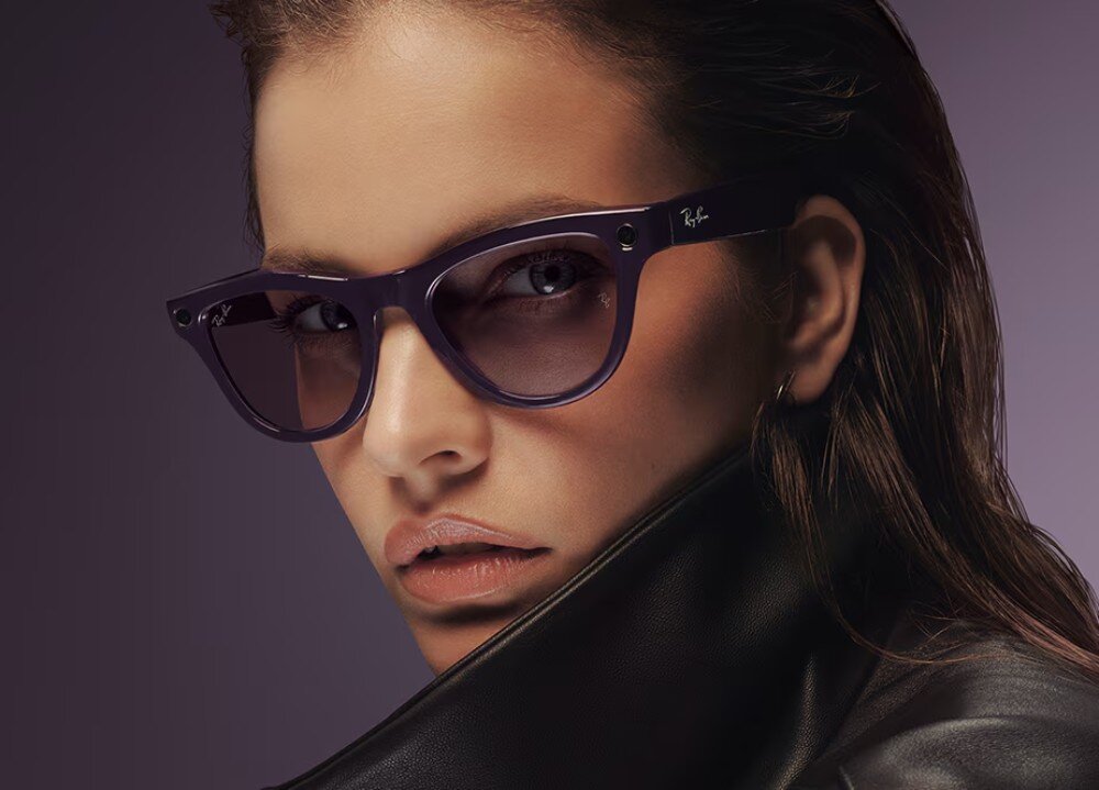 Osoba nosi okulary przeciwsłoneczne z ciemnymi oprawkami, na których widoczne jest logo \'Ray-Ban\'.