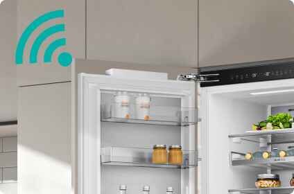 Otwarta lodówka z widocznymi półkami, na których znajdują się słoiki i pojemniki z jedzeniem. W lewym górnym rogu widoczna jest ikona sygnału Wi-Fi.
