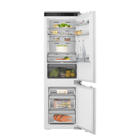 Otwarta lodówka z widocznymi półkami wypełnionymi różnymi produktami spożywczymi, takimi jak warzywa, napoje i opakowania z żywnością. Drzwi lodówki mają dodatkowe półki na butelki i drobne produkty.