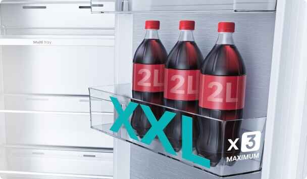 W lodówce znajdują się trzy butelki napoju o pojemności 2L każda, umieszczone w przezroczystej półce. Na obrazie widoczny jest napis \'XXL x3 MAXIMUM\'.