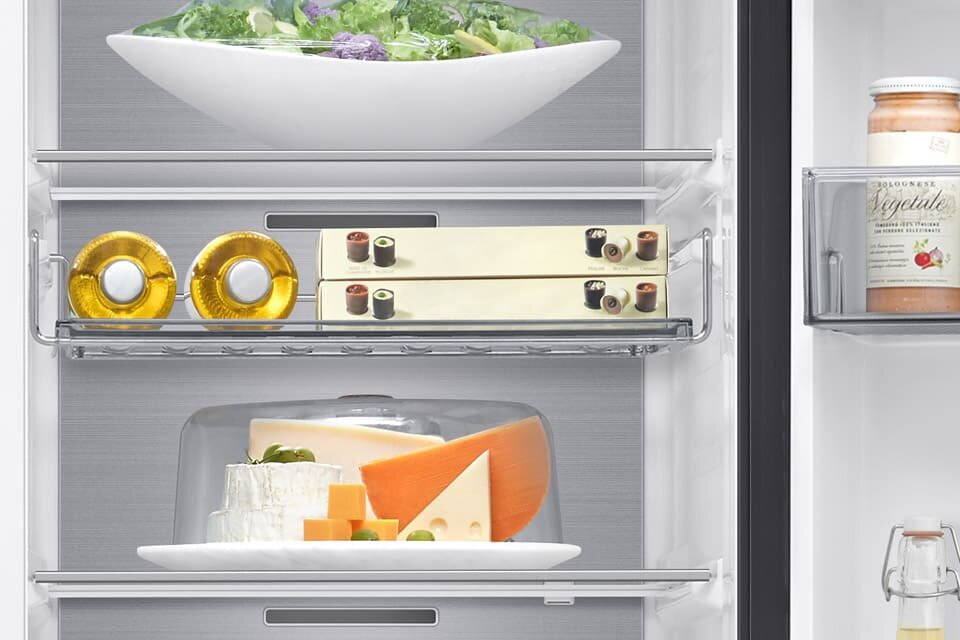 Wnętrze lodówki z półkami, na których znajdują się różne produkty spożywcze, w tym ser, sałatka i słoik z napisem \'Vegetables\'.