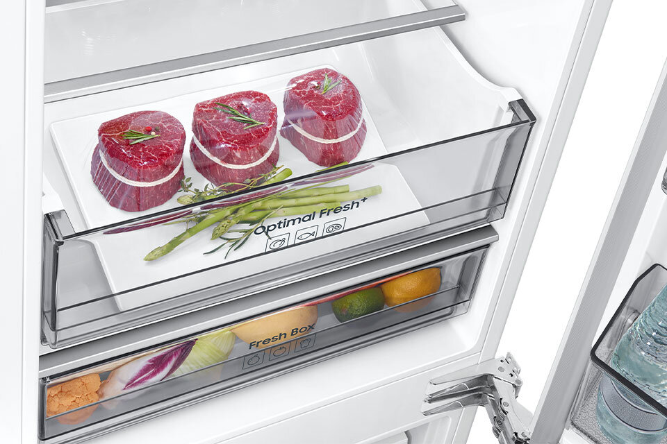 Wnętrze lodówki z widoczną szufladą oznaczoną jako \'Optimal Fresh+\', w której znajdują się trzy kawałki mięsa i kilka szparagów. Poniżej znajduje się szuflada \'Fresh Box\' z różnymi owocami i warzywami.