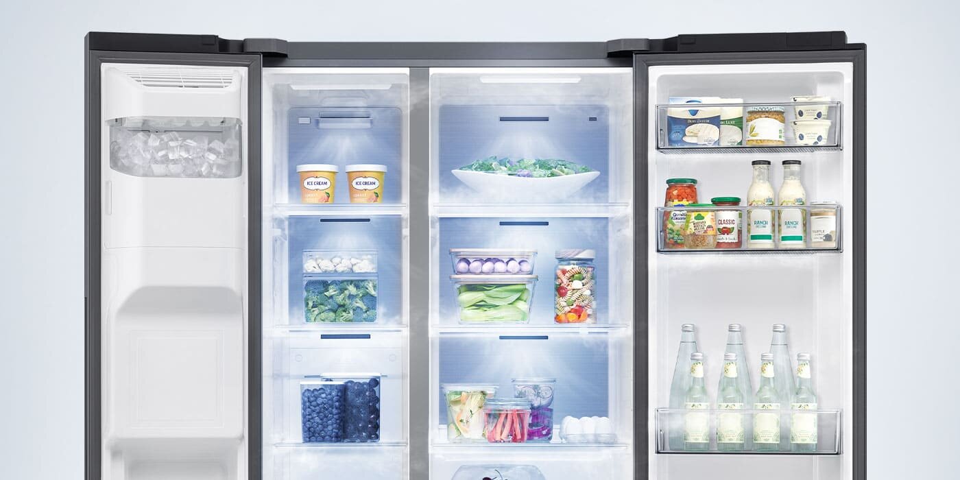 Wnętrze lodówki z widocznymi półkami wypełnionymi różnymi produktami spożywczymi, takimi jak warzywa, napoje i pojemniki z jedzeniem. Po lewej stronie znajduje się kostkarka do lodu.