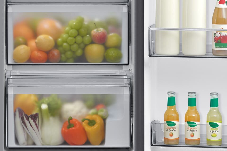 W lodówce znajdują się dwie szuflady z owocami i warzywami oraz półki z butelkami napojów. Na butelkach widoczny jest tekst \'Il Succo di Sicilia\'.