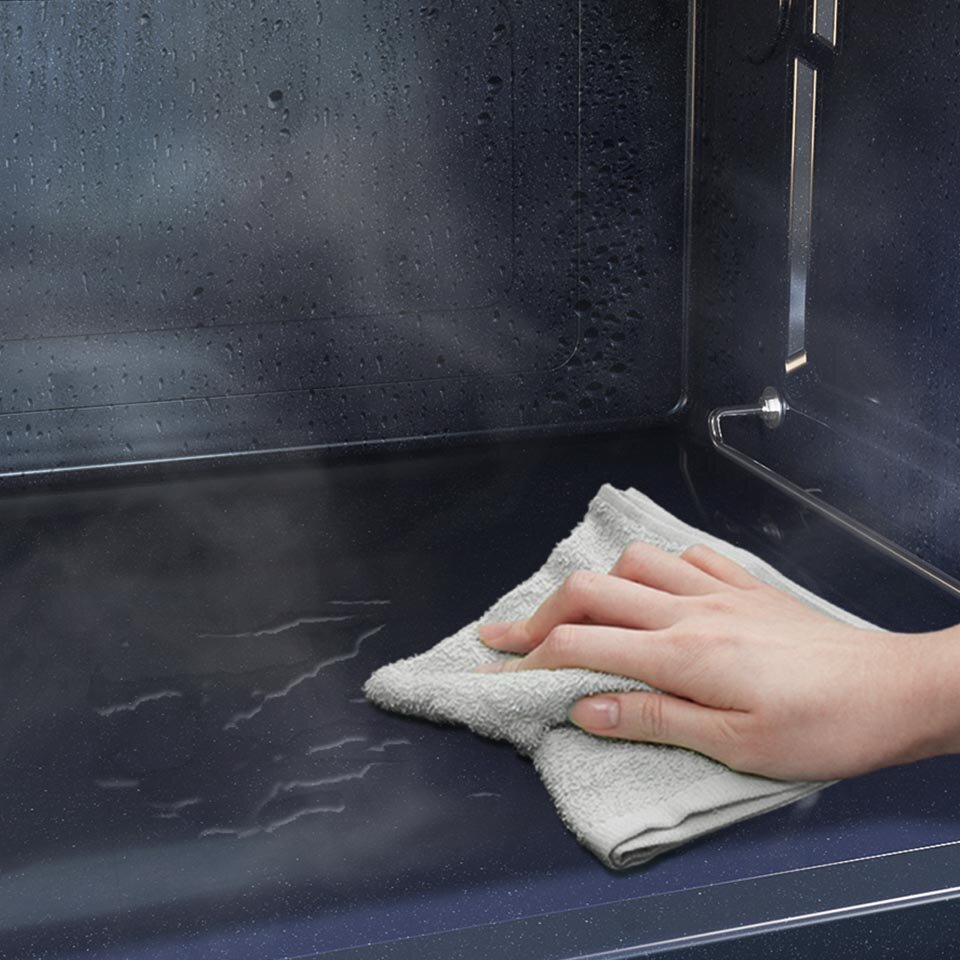 Wnętrze kuchenki mikrofalowej jest czyszczone wilgotną ściereczką, widoczna jest para i krople wody na ściankach.