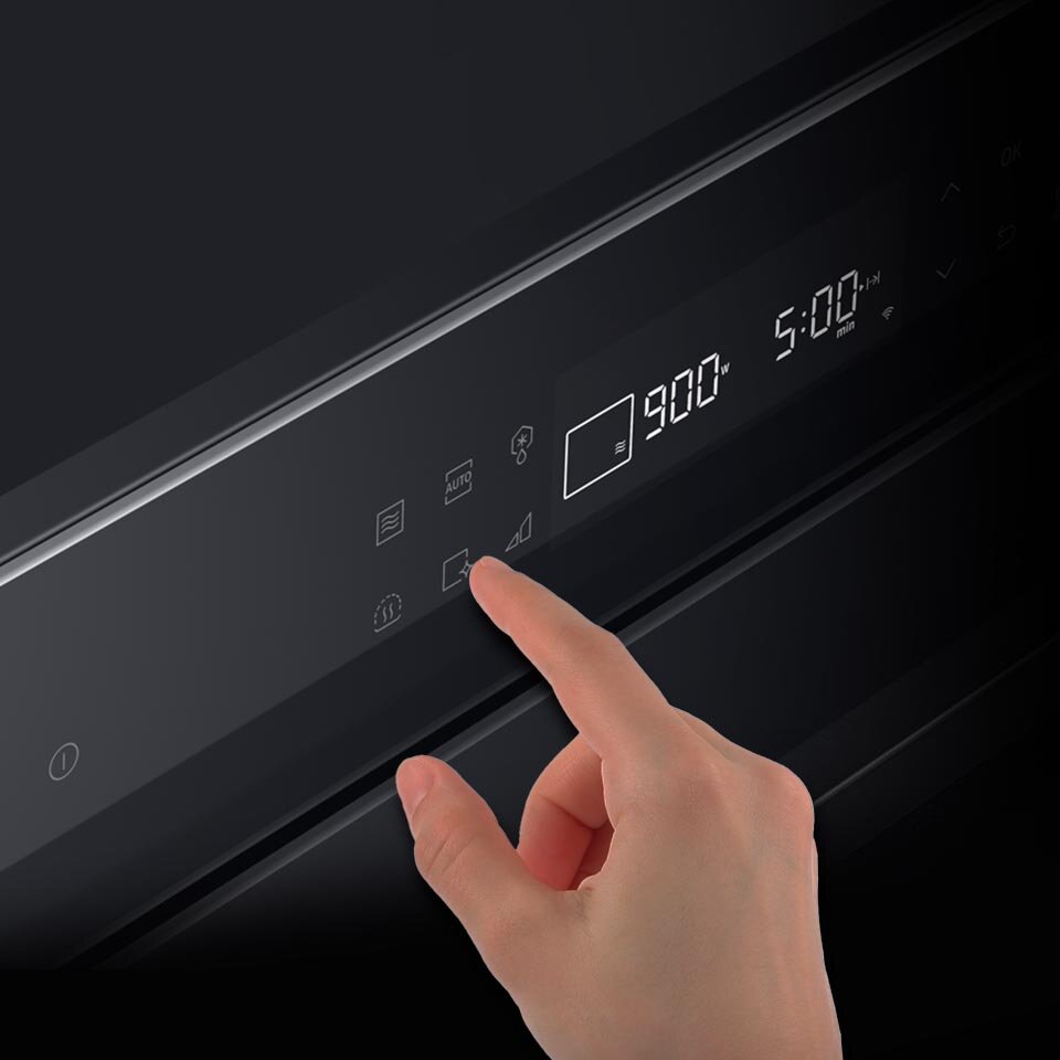Na obrazie widoczny jest panel dotykowy kuchenki mikrofalowej z wyświetlaczem pokazującym \'900 W\' i \'5:00 min\'. Dłoń dotyka jednego z przycisków na panelu.