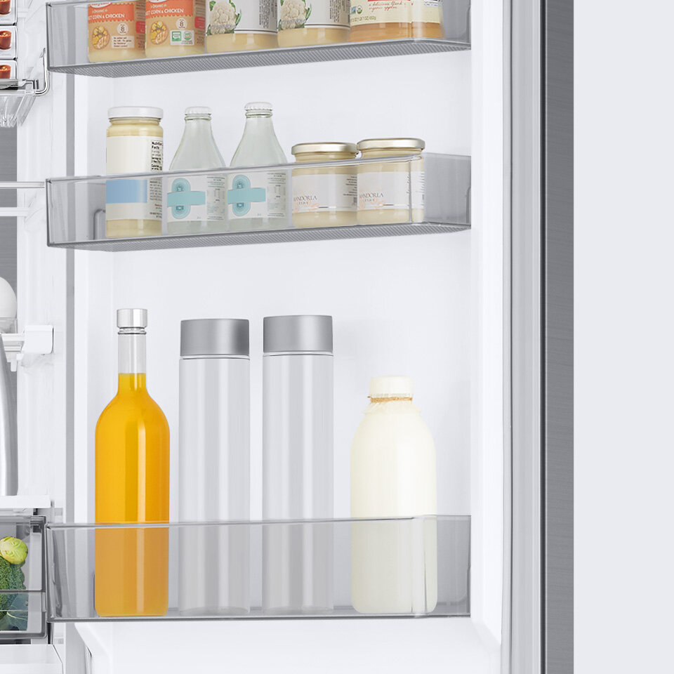 Wnętrze lodówki z trzema półkami na drzwiach, na których znajdują się różne produkty spożywcze, w tym butelki i słoiki. Widać także część wnętrza lodówki z warzywami w dolnej szufladzie.