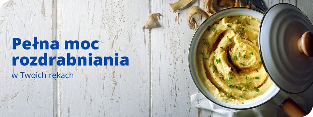 Na białym, drewnianym tle znajduje się garnek z kremową zupą posypaną szczypiorkiem. Obok widnieje tekst: \'Pełna moc rozdrabniania w Twoich rękach\'.