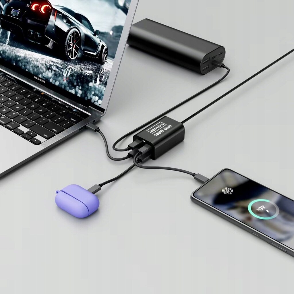 Na obrazie widać laptopa, powerbank, telefon i słuchawki podłączone do czarnej ładowarki z napisem \'Zenwire 100W GaN\'. Telefon pokazuje ekran ładowania z widocznym wskaźnikiem procentowym.