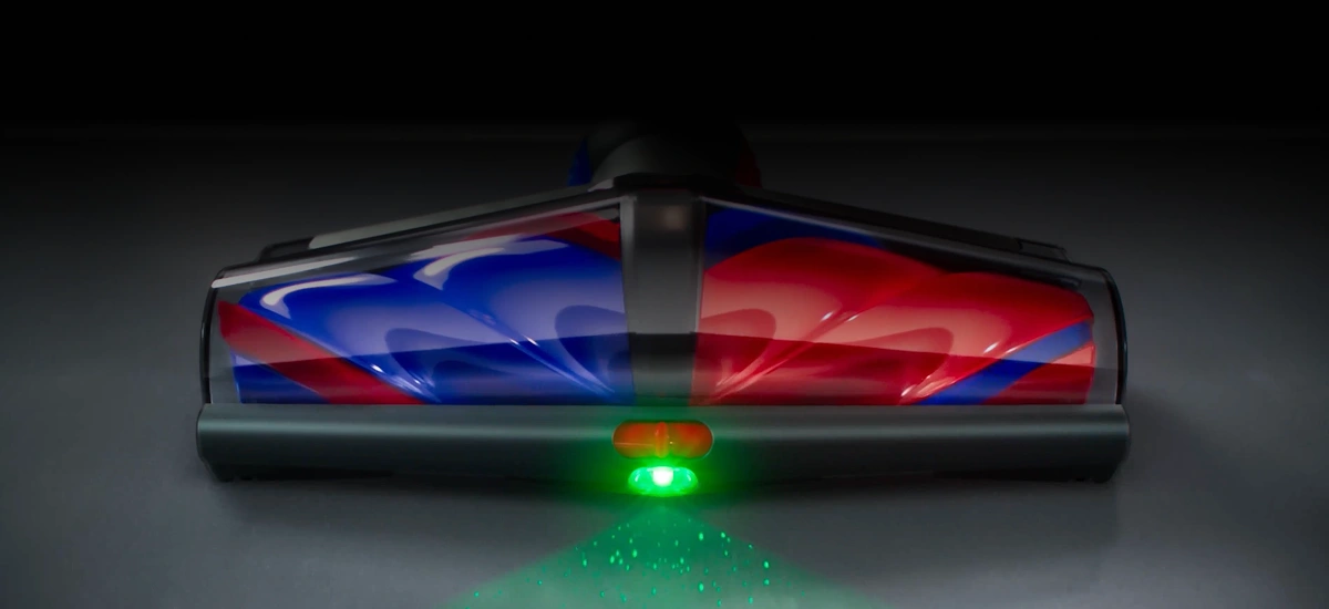 Głowica odkurzacza z kolorowymi elementami w odcieniach czerwieni i niebieskiego, z zielonym światłem emitowanym z przodu. Na ciemnym tle widoczny jest refleks świetlny na podłodze.