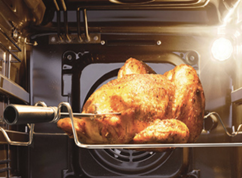 Wnętrze piekarnika z pieczonym kurczakiem na rożnie. W tle widoczne jest oświetlenie piekarnika.