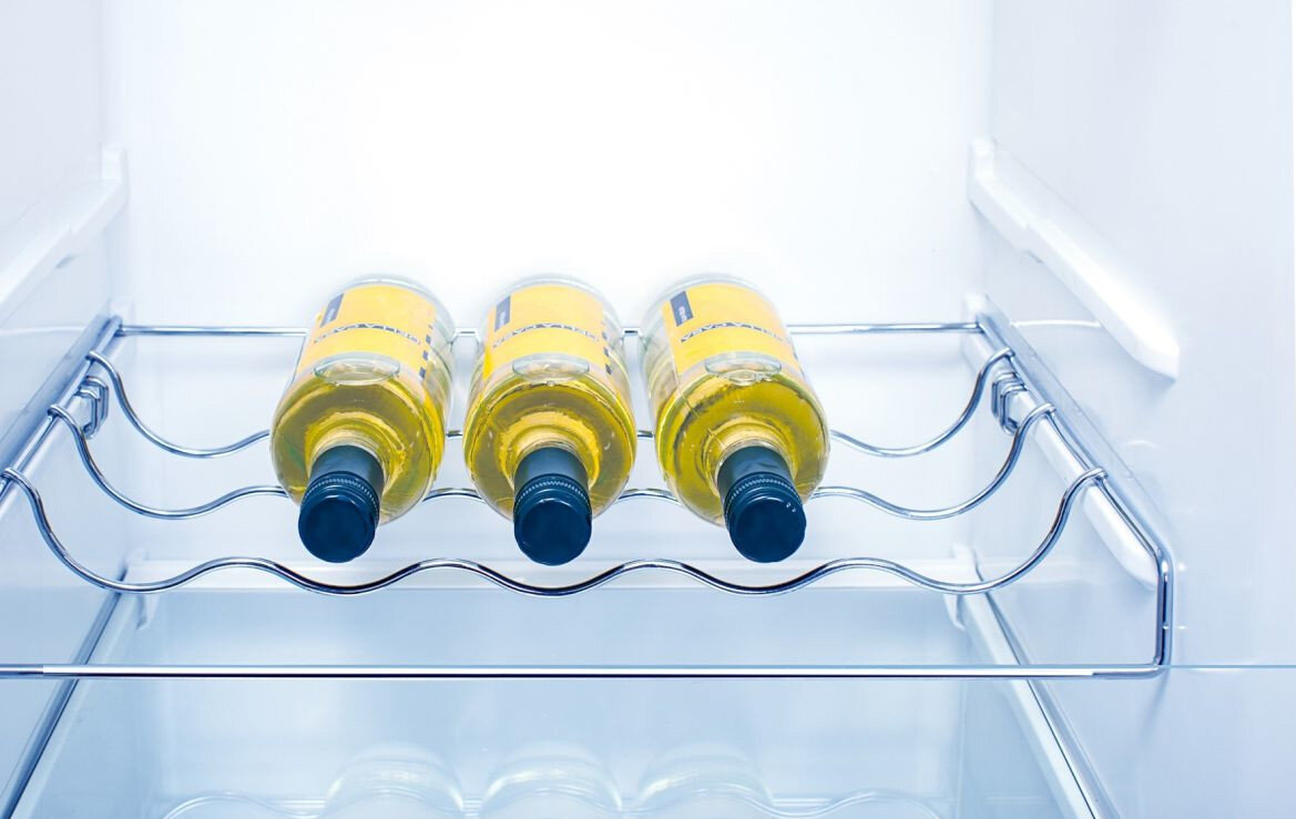 Wnętrze lodówki z trzema butelkami białego wina na metalowej półce. Butelki są ułożone poziomo.