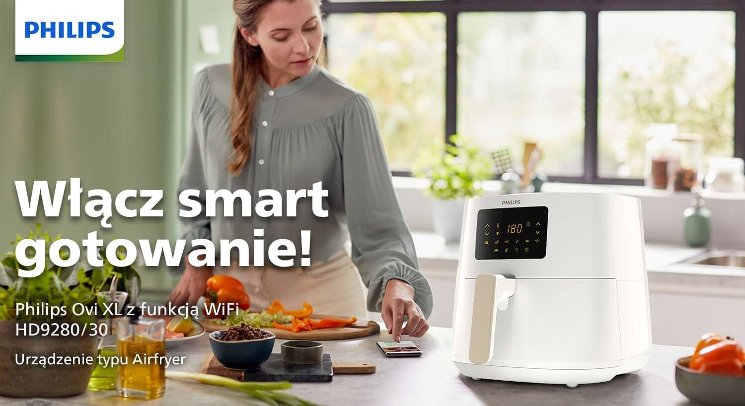 Na blacie kuchennym stoi biała frytkownica beztłuszczowa z wyświetlaczem cyfrowym. Obok znajduje się osoba przygotowująca jedzenie, a na obrazie widnieje tekst: \'Włącz smart gotowanie! Philips Ovi XL z funkcją WiFi HD9280/30 Urządzenie typu Airfryer\'.