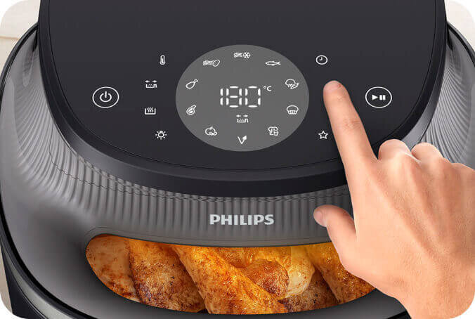 Na zdjęciu widać frytkownicę beztłuszczową marki PHILIPS z wyświetlaczem dotykowym, na którym widoczna jest temperatura 180°C. W dolnej części urządzenia znajdują się pieczone ziemniaki.