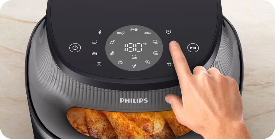 Na obrazie widoczna jest frytkownica beztłuszczowa marki PHILIPS z panelem dotykowym, na którym wyświetlana jest temperatura 180°C. Wewnątrz urządzenia znajdują się pieczone frytki.