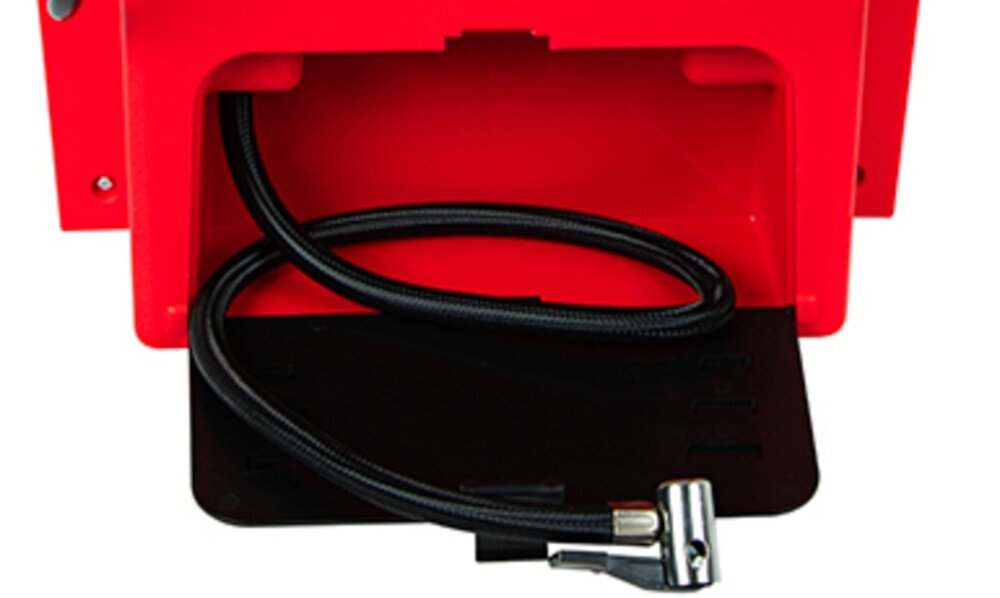 Czerwone urządzenie z otwartą komorą, w której znajduje się czarny przewód zakończony metalowym złączem. Widoczne są również metalowe śruby na obudowie.