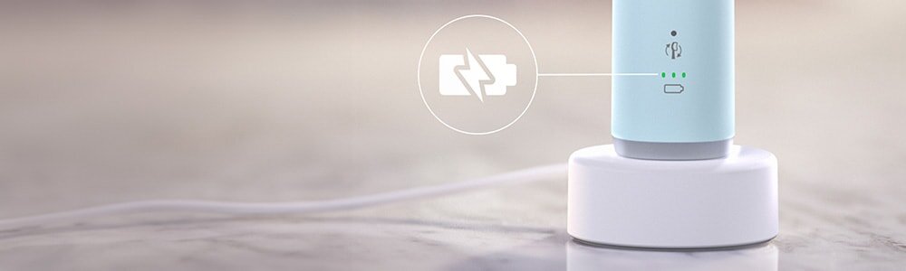 Na obrazie widoczna jest niebieska szczoteczka soniczna umieszczona na białej podstawce ładującej. Obok znajduje się symbol baterii z ikoną ładowania oraz trzy zielone diody wskazujące poziom naładowania.