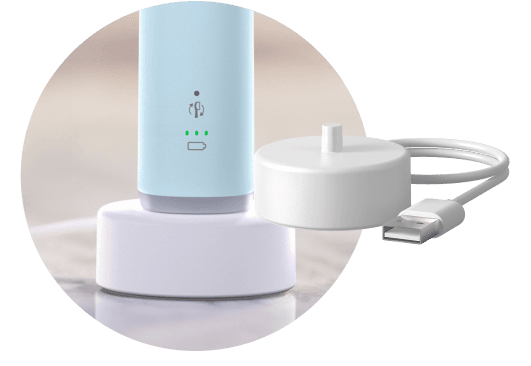 Na obrazie widoczna jest niebieska szczoteczka soniczna stojąca na białej podstawce ładującej. Obok znajduje się biały kabel USB z okrągłą końcówką ładującą.