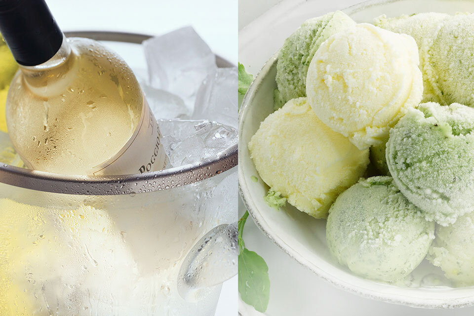 Po lewej stronie znajduje się butelka białego wina w wiaderku z lodem. Po prawej stronie widoczna jest miska z kulkami lodów w kolorach zielonym i żółtym.