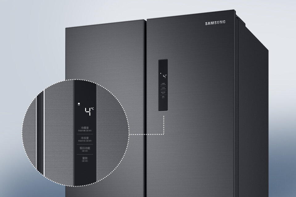 Grafitowa lodówka z dwoma drzwiami, na jednym z nich widoczny jest panel z wyświetlaczem pokazującym temperaturę 4°C. Na drzwiach znajduje się logo \'SAMSUNG\'.