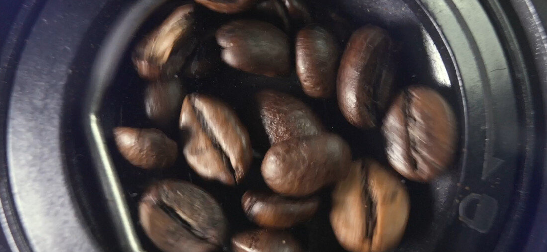 Zbliżenie na ciemne ziarna kawy w okrągłym pojemniku.