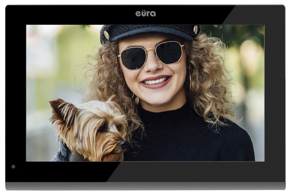 Na ekranie urządzenia z logo \'eura\' widoczna jest kobieta w okularach przeciwsłonecznych i czapce, trzymająca małego psa. Tło jest rozmyte, co sugeruje zewnętrzne otoczenie.