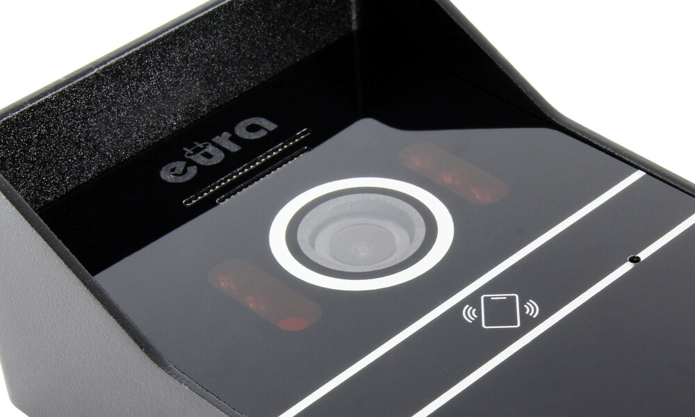 Czarny wideodomofon z widocznym obiektywem kamery i logo \'eura\' na obudowie. Obok obiektywu znajdują się dwa czerwone elementy oraz symbol karty z falami sugerujący funkcję zbliżeniową.