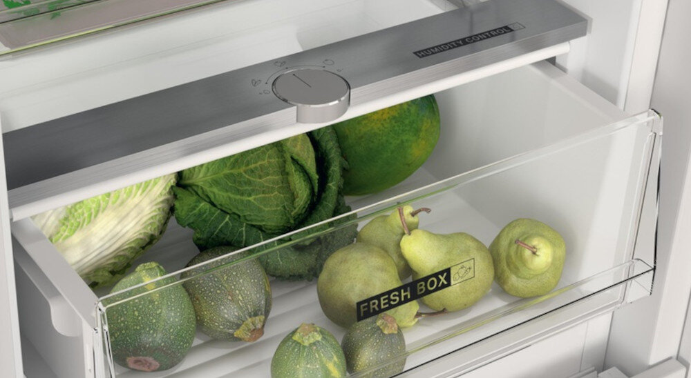 Wnętrze lodówki z szufladą oznaczoną napisem \'FRESH BOX\', w której znajdują się warzywa i owoce, takie jak kapusta, cukinia i gruszki. Na górze widoczny jest panel z pokrętłem i napisem \'HUMIDITY CONTROL\'.