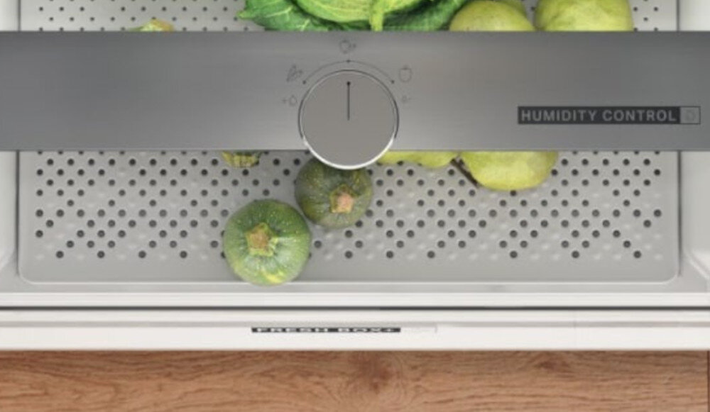 Wnętrze lodówki z szufladą na warzywa, w której znajdują się zielone warzywa. Na szufladzie widoczny jest napis \'HUMIDITY CONTROL\'.