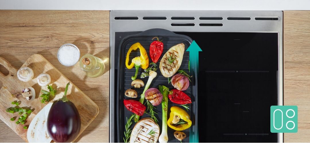 KUCHNIA GORENJE MEKIS5101I Widok z góry na płytę grzejną z żeliwną patelnią grillową pełną kolorowych grillowanych warzyw, ustawioną częściowo na strefie indukcyjnej obok drewnianego blatu z deską, bakłażanem i przyprawami, a turkusowa strzałka w górę podkreśla możliwość rozszerzenia pola gotowania (łączone strefy) BridgeZone duża powierzchnia