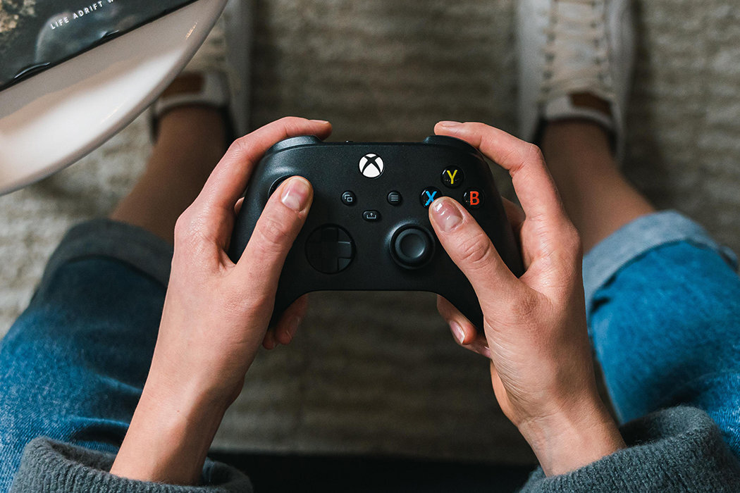 Osoba trzyma czarny kontroler do gier z widocznym logo Xbox. Na kontrolerze znajdują się kolorowe przyciski oznaczone literami Y, X, B, A.