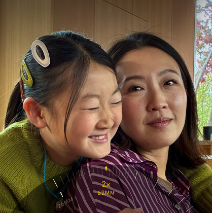 Dwie osoby pozują do zdjęcia w pomieszczeniu z drewnianymi panelami. Na zdjęciu widoczne są cyfry i symbole: \'1x\', \'2x\', \'26MM\', \'52MM\'.