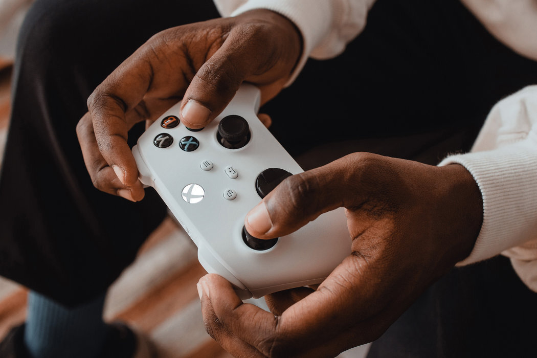 Osoba trzyma biały kontroler do gier z widocznym logo Xbox. Kontroler ma czarne przyciski i gałki analogowe.