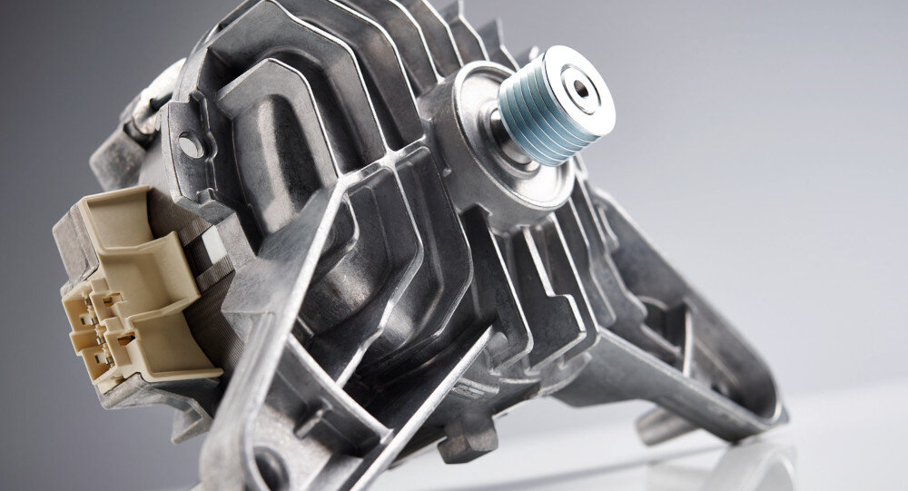 Zdjęcie przedstawia metalowy element mechaniczny z widocznymi żebrami chłodzącymi i niebieskim elementem na końcu. W tle znajduje się szare tło.