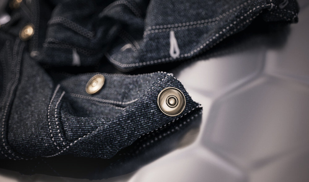 Fragment materiału z metalowymi guzikami leży na powierzchni o heksagonalnym wzorze.