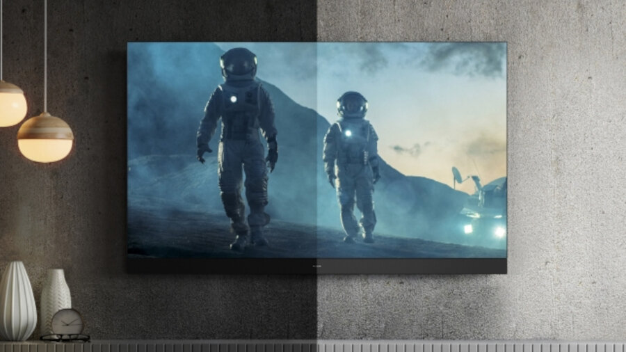 Telewizor wyświetla obraz dwóch astronautów na tle górskiego krajobrazu, z wyraźnym podziałem na jaśniejszą i ciemniejszą stronę ekranu. W tle widoczne są lampy i dekoracje na półce.