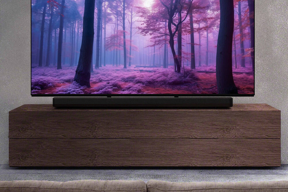 Na drewnianej szafce stoi telewizor z wyświetlonym obrazem lasu w odcieniach fioletu i różu. Przed telewizorem znajduje się czarny soundbar.