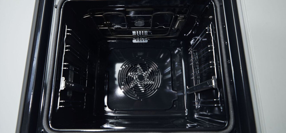 Wnętrze czarnego piekarnika z widocznym wentylatorem na tylnej ścianie oraz metalowymi prowadnicami po bokach.