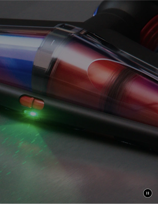 Zbliżenie na część odkurzacza z przezroczystym pojemnikiem, w którym widać kolorowe elementy. Na obudowie znajduje się zielona dioda i czerwony przycisk.